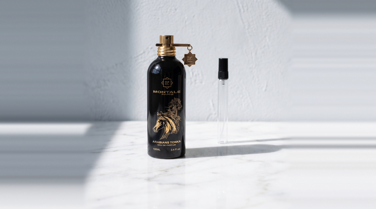 Botella original de Montale Arabians Tonka junto a un decant de vidrio sobre mármol blanco