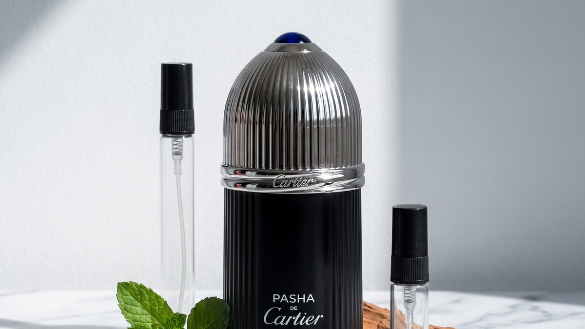 Decants de Cartier: la botella negra estriada de Pasha Edition Noire junto a tres atomizadores de vidrio sobre marmol