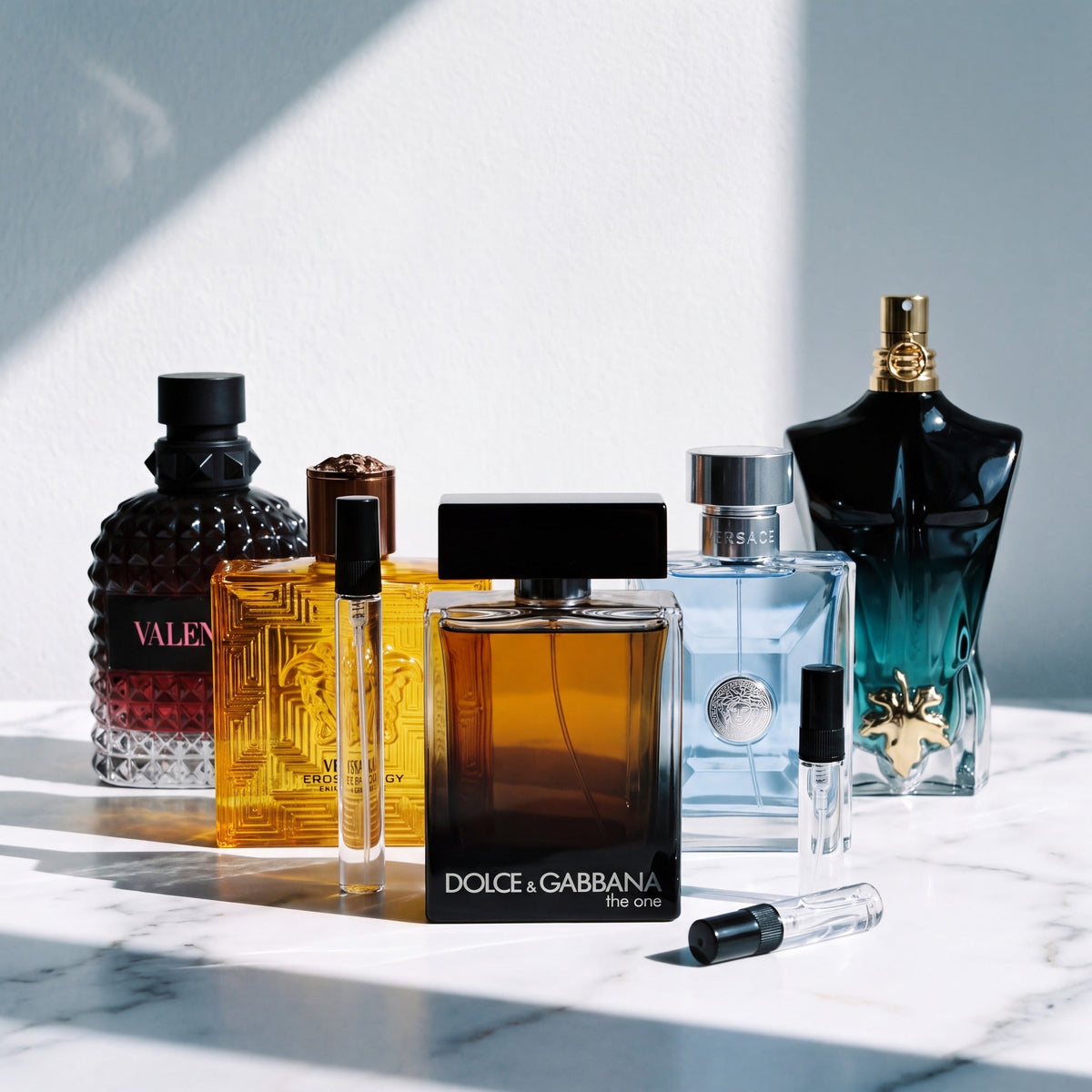 Packs de decants: cinco perfumes de disenador junto a los atomizadores de vidrio sobre marmol blanco