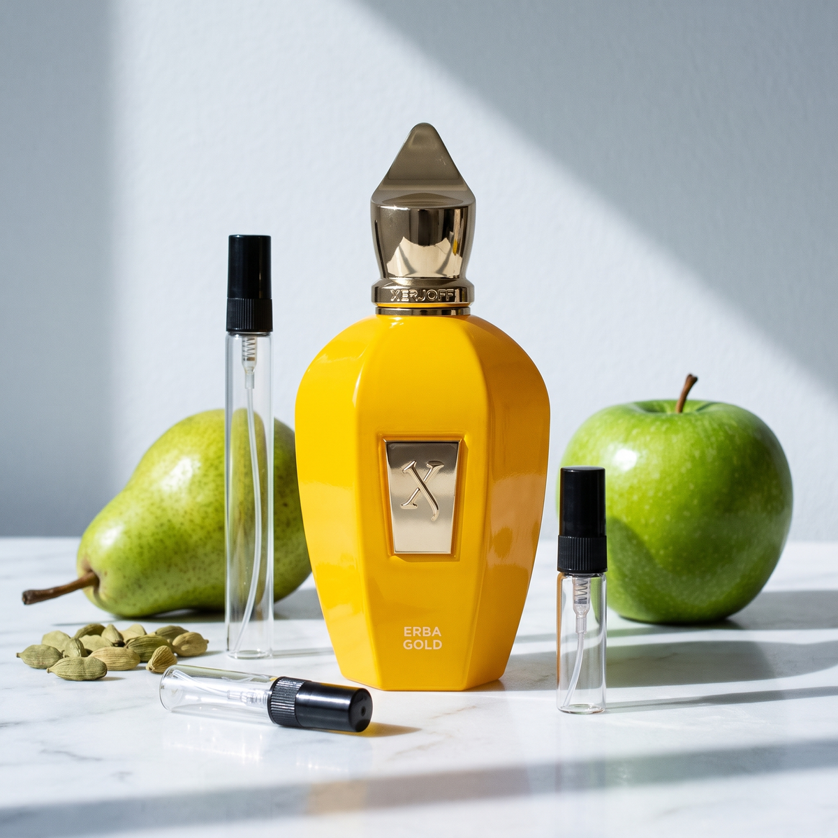 Decant de Xerjoff Erba Gold en 3, 5 y 10 ml junto a la botella amarilla original de Xerjoff con pera, manzana verde y vainas de cardamomo