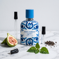 Decant de Dolce & Gabbana Light Blue Capri In Love Pour Homme en 3, 5 y 10 ml junto a la botella blanca con mayolica azul original de Dolce & Gabbana con un higo verde partido, pimienta negra y hojas de pachuli