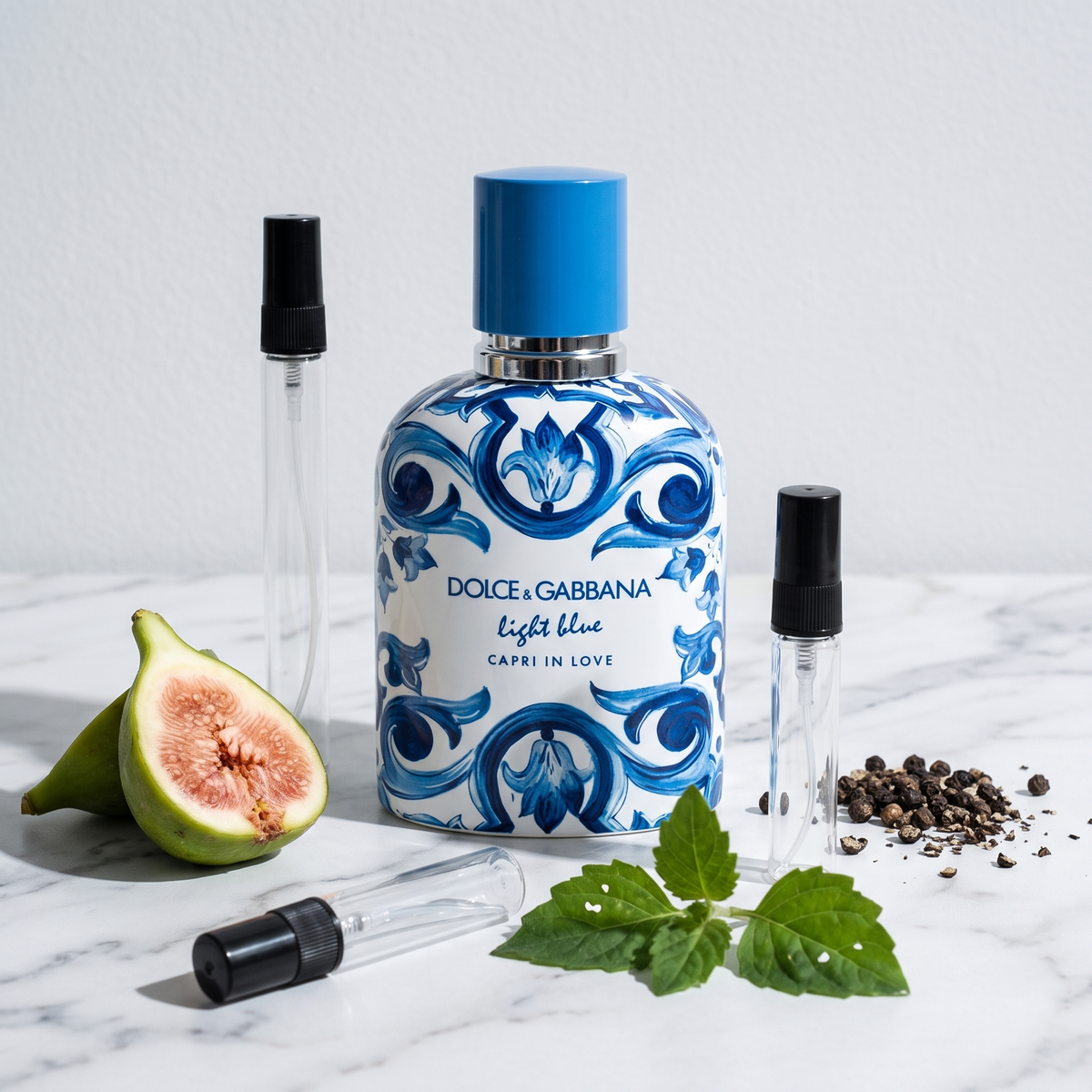 Decant de Dolce & Gabbana Light Blue Capri In Love Pour Homme en 3, 5 y 10 ml junto a la botella blanca con mayolica azul original de Dolce & Gabbana con un higo verde partido, pimienta negra y hojas de pachuli