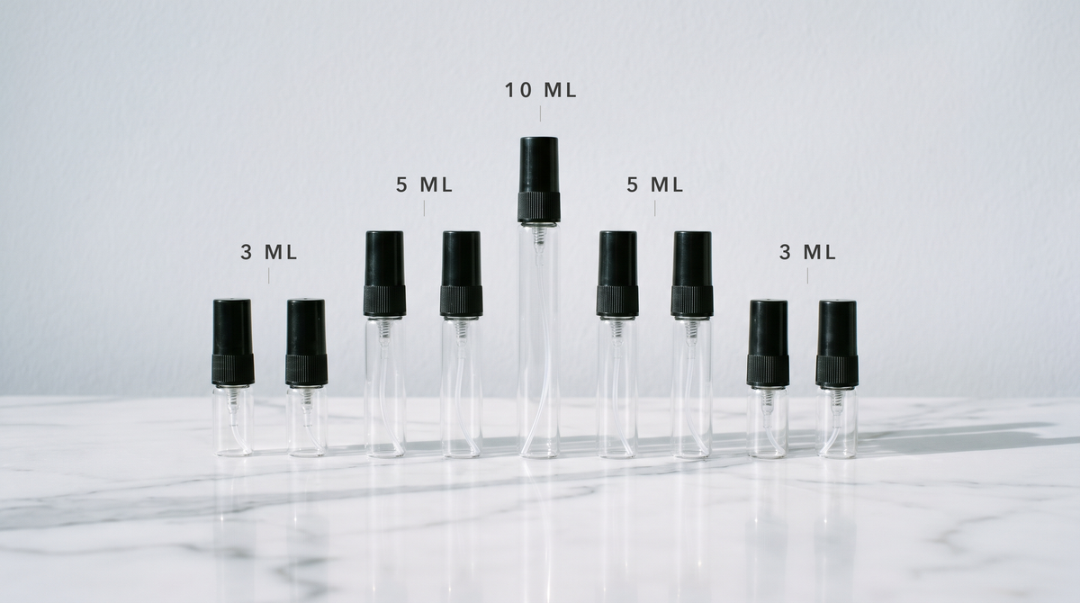 Atomizadores de vidrio vacíos ordenados en escalera y rotulados 3 ml, 5 ml y 10 ml sobre mármol